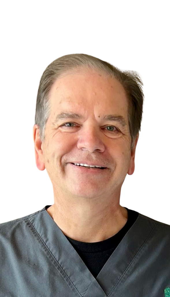 Portrait of a smiling middle-aged clinician wearing gray scrubs against a white background, facing the camera.